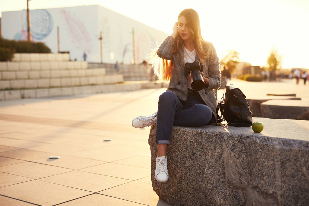 Fotograf dziewczyny siedzą na ar rock i wygląd jej aparat fotograficzny - Zdjęcie, obraz