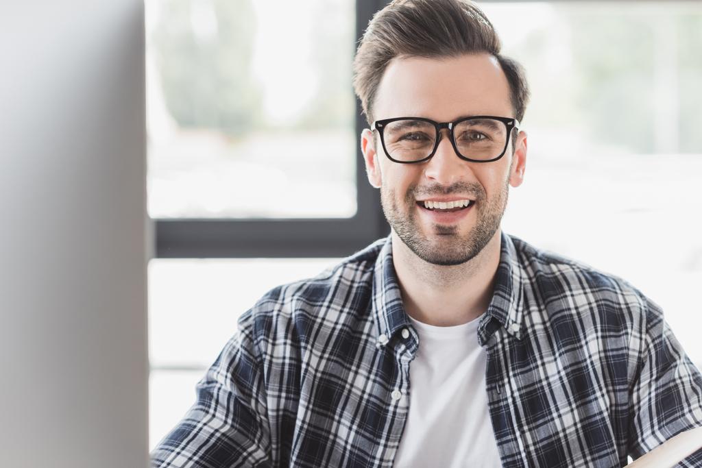csinos, fiatal férfi a szemüvegek mosolyogva kamera munkahelyen portréja - Fotó, kép