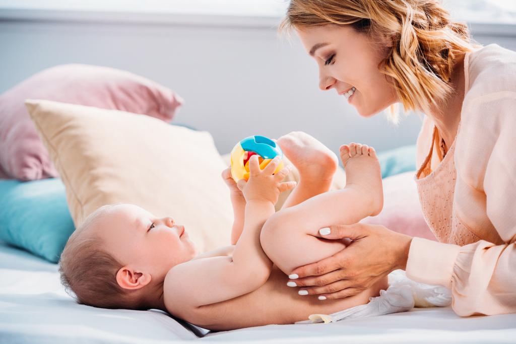 happy mother putting diaper on little child while he playing with toy - Photo, Image
