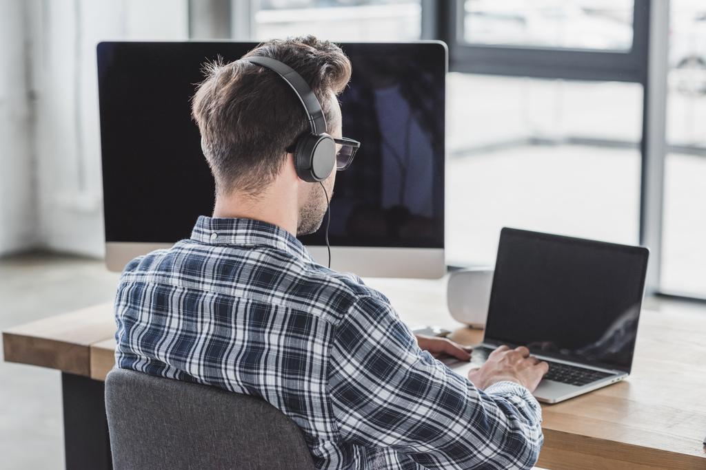 visão traseira do programador jovem em fones de ouvido e óculos que trabalham com laptop
 - Foto, Imagem