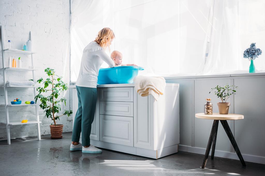 moeder haar kindje in kunststof baby badkuip thuis wassen - Foto, afbeelding