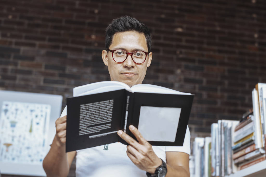 Giovane uomo dagli occhiali che tiene un libro in una libreria
. - Foto, immagini
