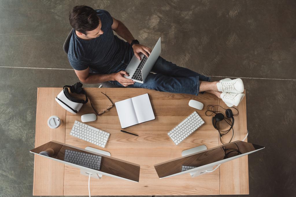 vista aérea del hombre joven utilizando computadoras portátiles y de escritorio en el lugar de trabajo
  - Foto, imagen
