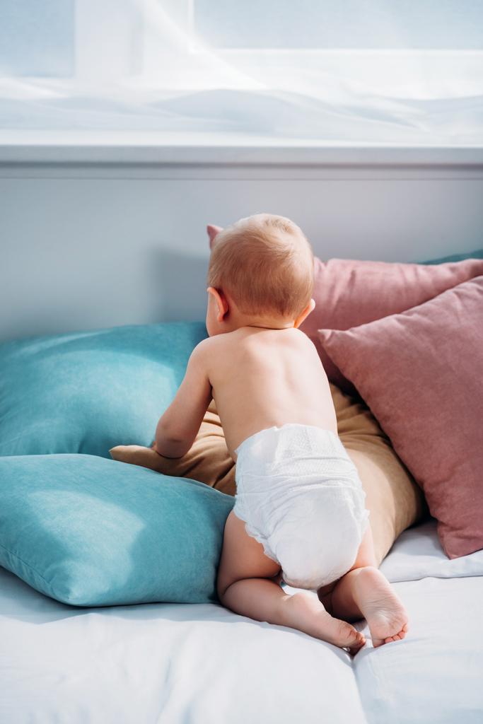 rear view of little baby crawling on bed with lot of pillows - Photo, Image