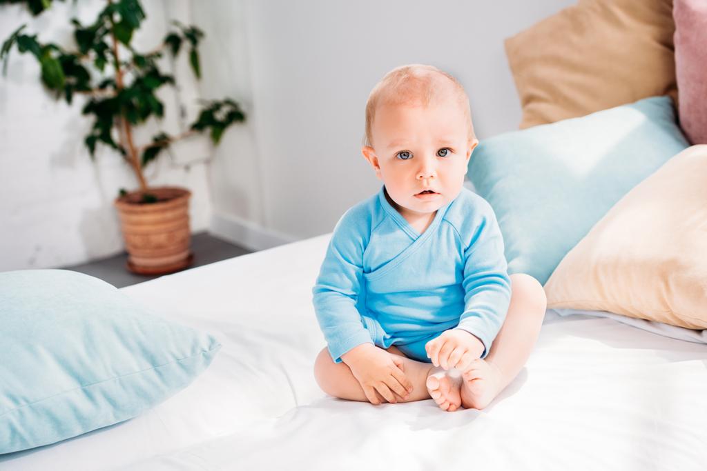 yatağa evde oturan ve kameraya bakarak küçük bebek - Fotoğraf, Görsel