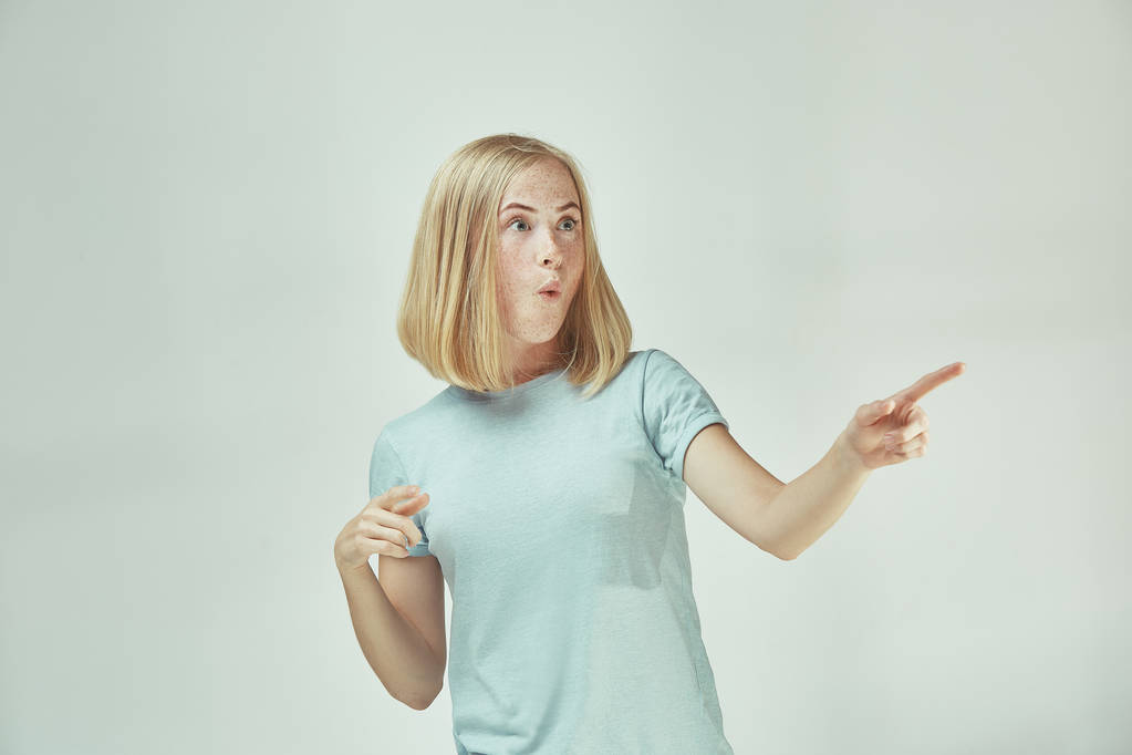 Η νεαρή γυναίκα ψιθυρίζει ένα μυστικό πίσω από το χέρι της πάνω από το γκρίζο φόντο - Φωτογραφία, εικόνα