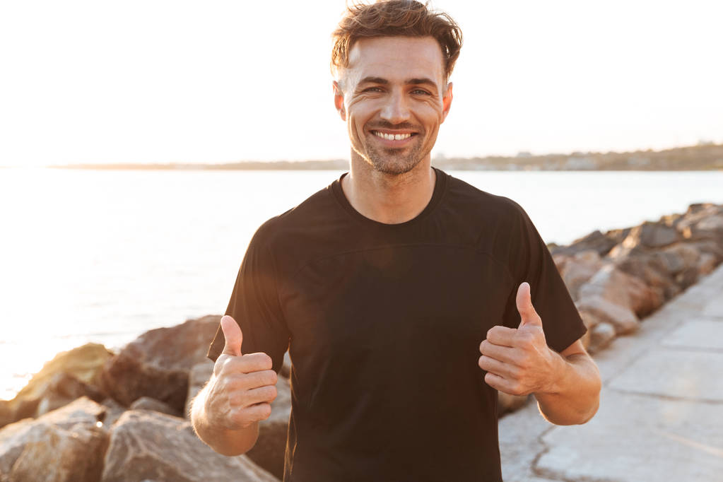 Portrait of a cheerful sportsman celebrating success and showing thumbs up outdoors - Photo, Image
