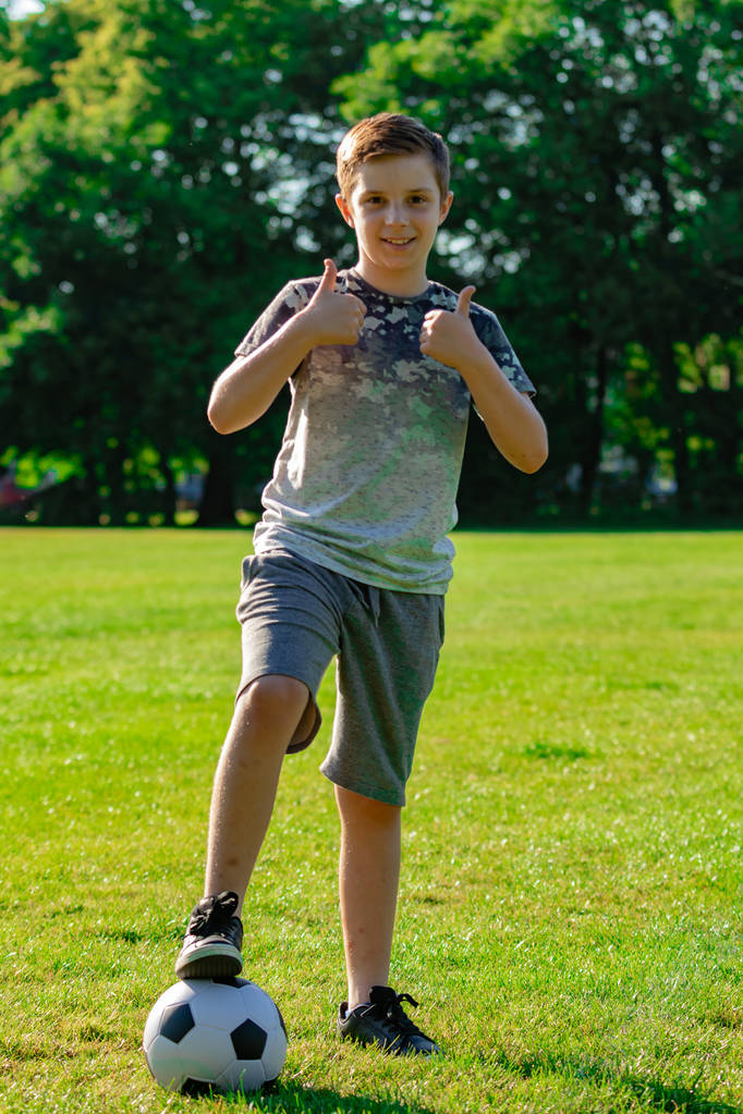 Rapaz pré-adolescente com uma bola de futebol num parque
 - Foto, Imagem