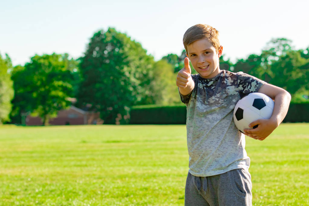 Wstępnie teen chłopiec trzyma piłkę nożną w parku - Zdjęcie, obraz