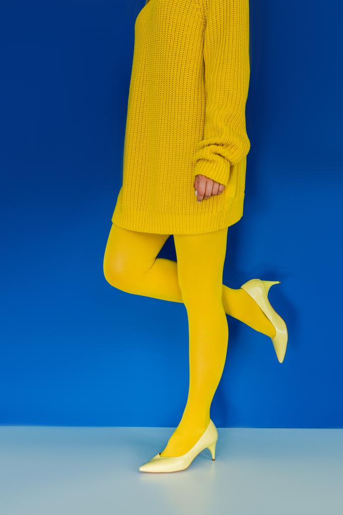 Ausgeschnittene Ansicht eines Mädchens in gelben Kleidern und hochhackigen Schuhen auf blauem Hintergrund - Foto, Bild