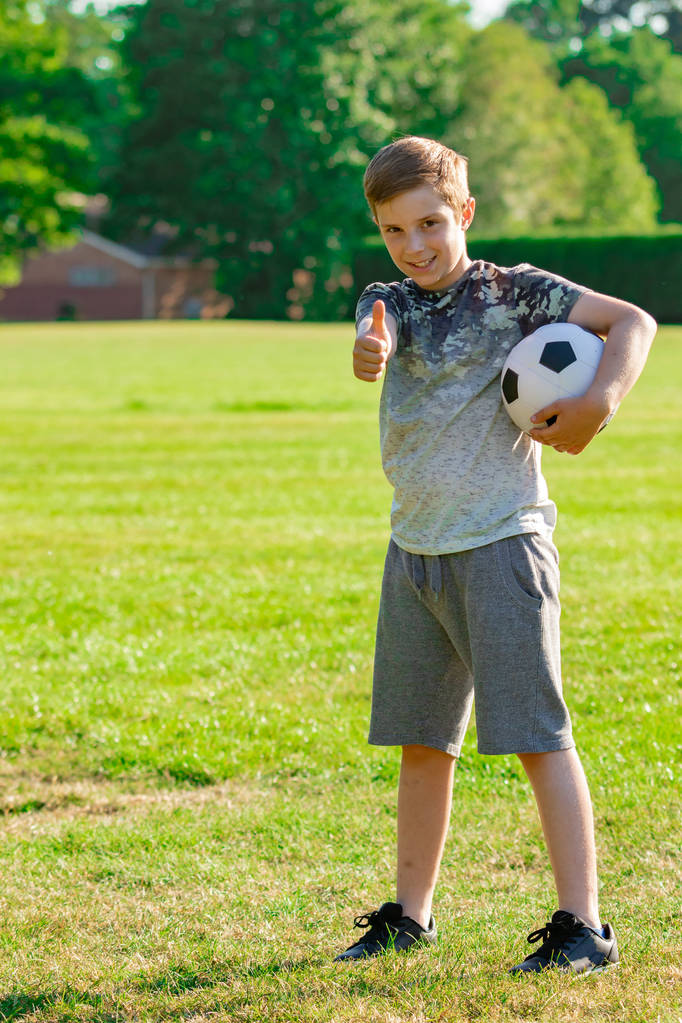 Wstępnie teen chłopiec trzyma piłkę nożną w parku - Zdjęcie, obraz