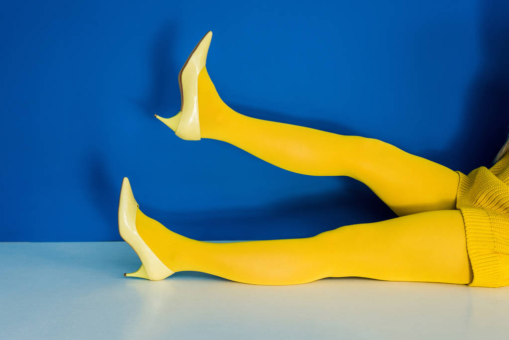 Przycięte widzenia kobiece nogi w żółte buty i rajstopy na niebieskim tle - Zdjęcie, obraz