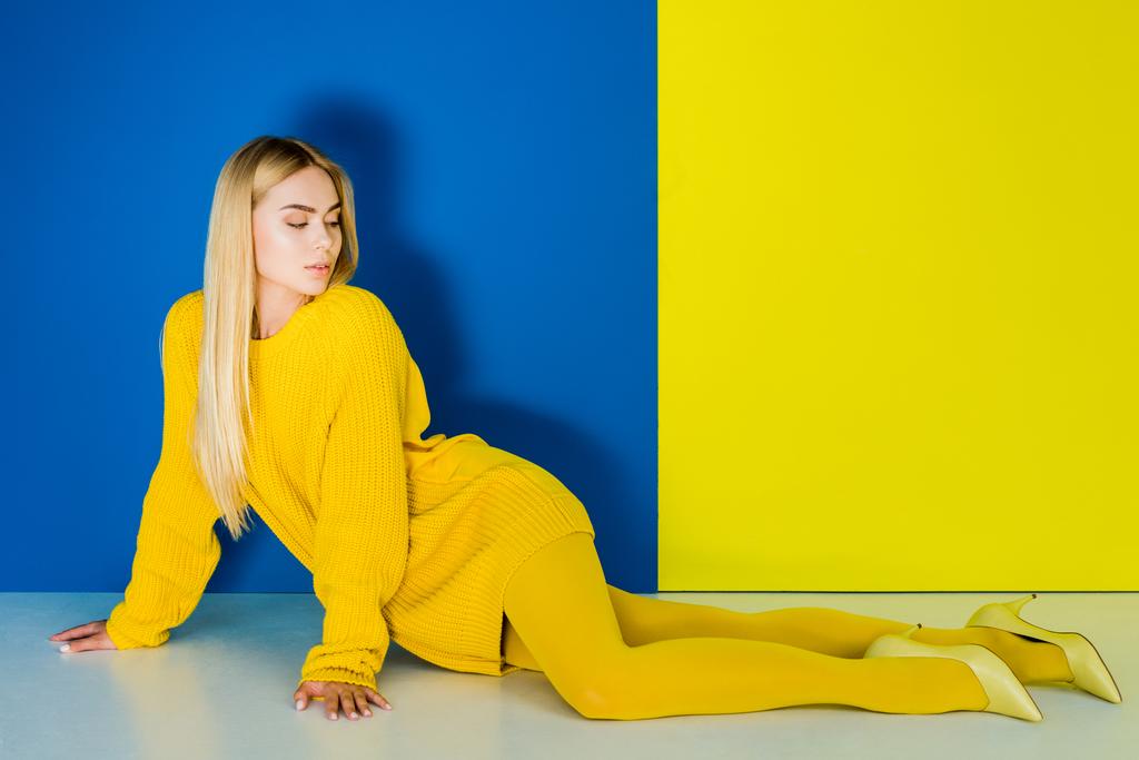 Elegant blonde woman all dressed in yellow posing on blue and yellow background - Photo, Image