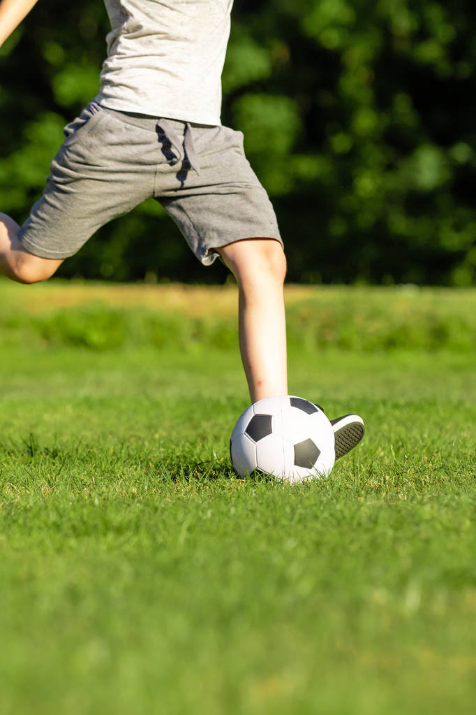Προ-έφηβος αγόρι παίζει με μια μπάλα ποδοσφαίρου σε ένα πάρκο - Φωτογραφία, εικόνα