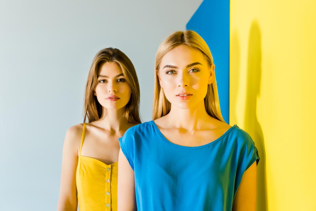 Όμορφη μελαχρινή και Ξανθιά κορίτσια ποζάρουν σε μπλε και κίτρινο φόντο - Φωτογραφία, εικόνα