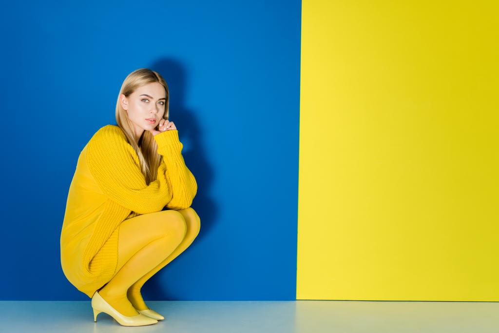 Модель жіночої моди в жовтому вбранні, що сидить на синьо-жовтому фоні
 - Фото, зображення