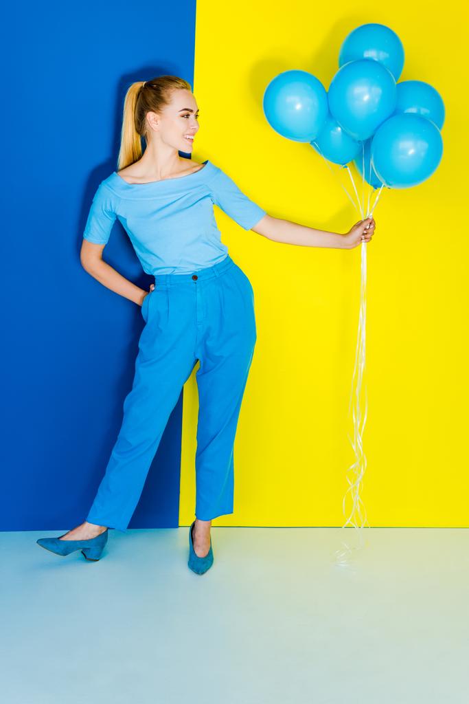 Bella donna bionda che tiene mazzo di palloncini blu su sfondo blu e giallo
 - Foto, immagini