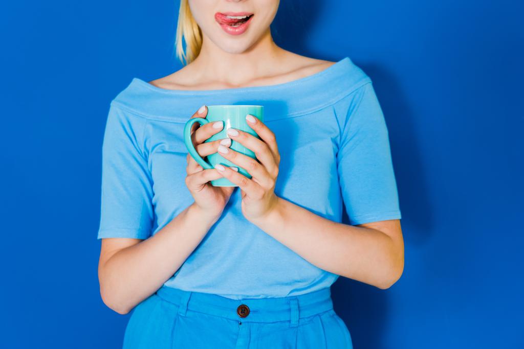 Rapariga atraente em roupas azuis com copo azul nas mãos sobre fundo azul
 - Foto, Imagem