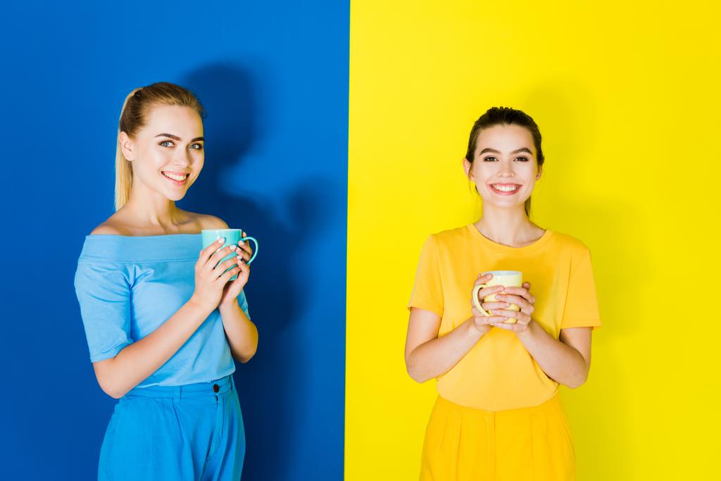 Смолящие стильные женщины, держащие чашки на синем и желтом фоне
 - Фото, изображение