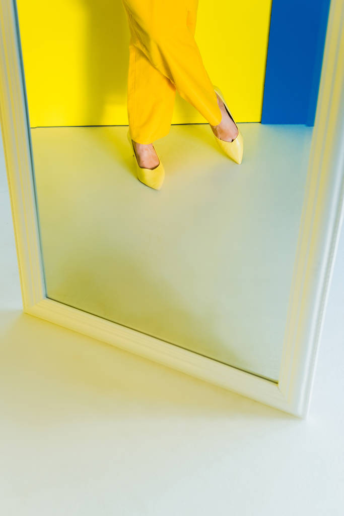 Ausgeschnittene Ansicht weiblicher Füße im Spiegel auf blauem und gelbem Hintergrund - Foto, Bild