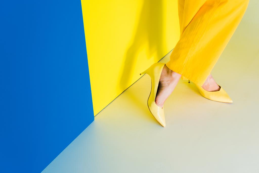 Cropped view of female feet in heeled shoes on blue and yellow background - Photo, Image