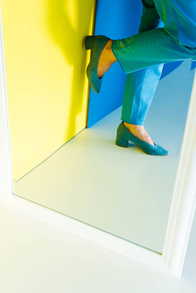 Bijgesneden beeld van vrouwelijke voeten in blauwe hakken op blauwe en gele achtergrond - Foto, afbeelding