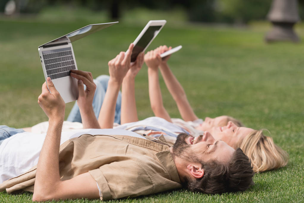счастливая семья лежит на траве и с помощью цифровых устройств
 - Фото, изображение
