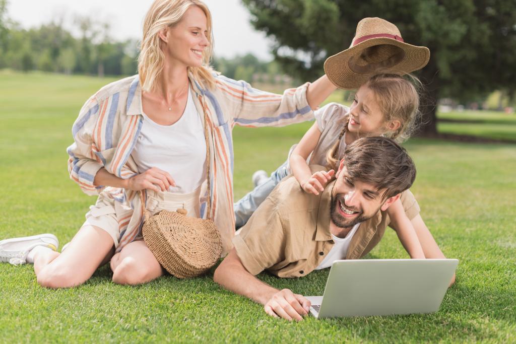 Szczęśliwa rodzina korzysta z laptopa podczas wspólnie spędzać czas w parku - Zdjęcie, obraz