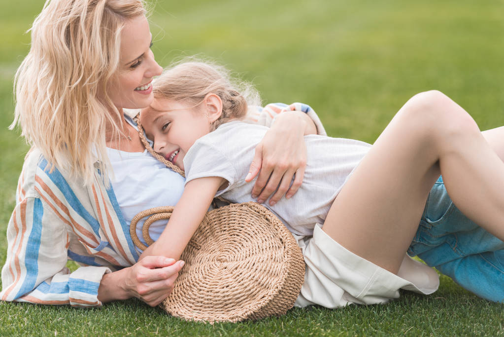 schöne glückliche Mutter und Tochter, die sich auf dem grünen Rasen umarmen - Foto, Bild