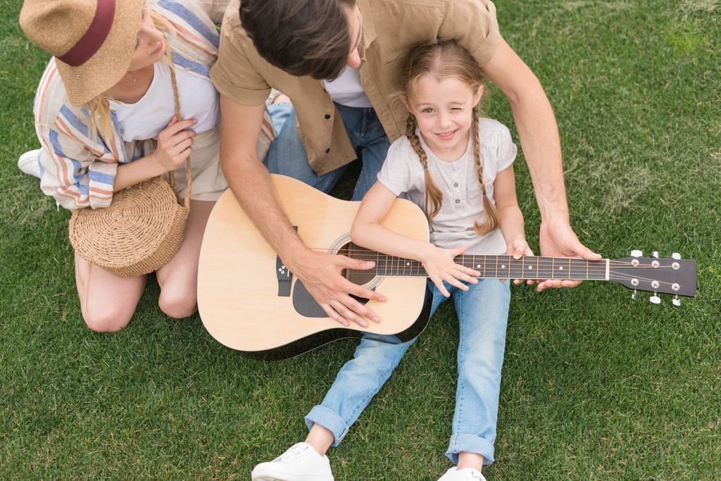 pohled na rodinu s jedním dítětem hrál na akustickou kytaru na louce - Fotografie, Obrázek