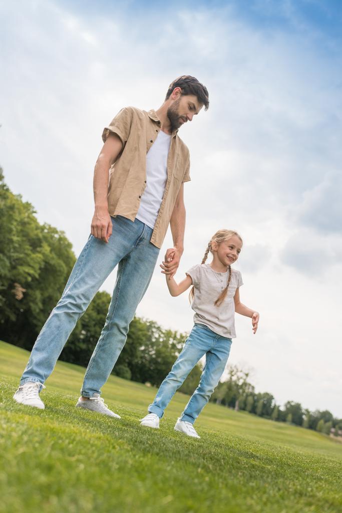 vista de ángulo bajo del padre y la pequeña hija tomados de la mano mientras pasan tiempo juntos en el parque
 - Foto, imagen
