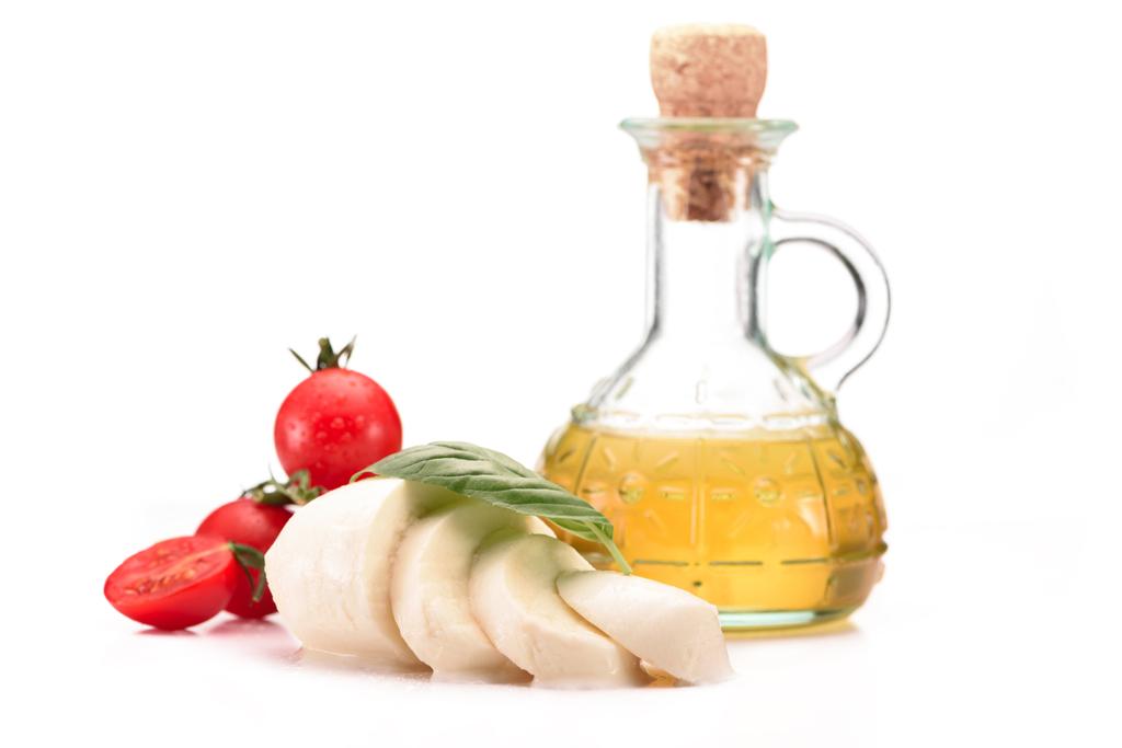 close up view of arranged glass bottle with oil, cherry tomatoes and mozzarella cheese with basil leaves isolated on white - Photo, Image