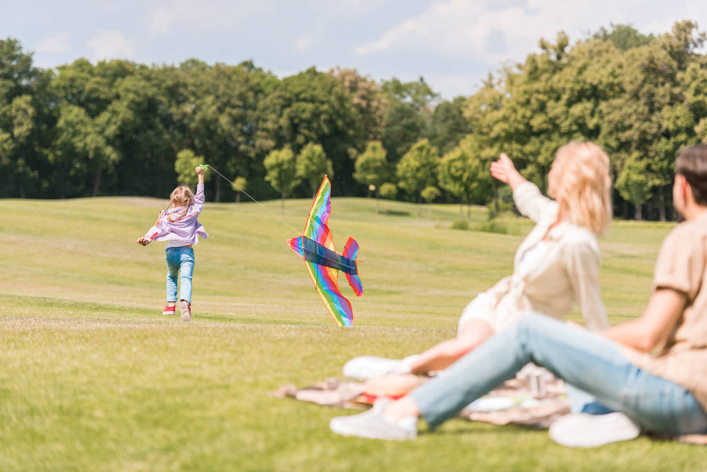 Οι γονείς βλέπουν κόρη παίζει με πολύχρωμα χαρταετού στο πάρκο  - Φωτογραφία, εικόνα