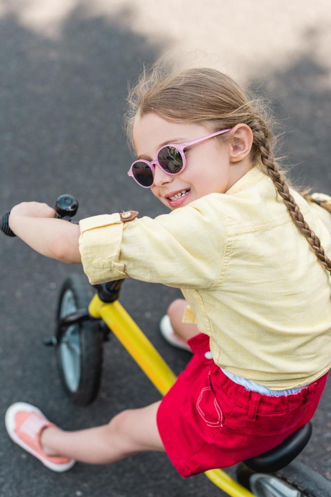 adorabile bambino sorridente in occhiali da sole in bicicletta
  - Foto, immagini