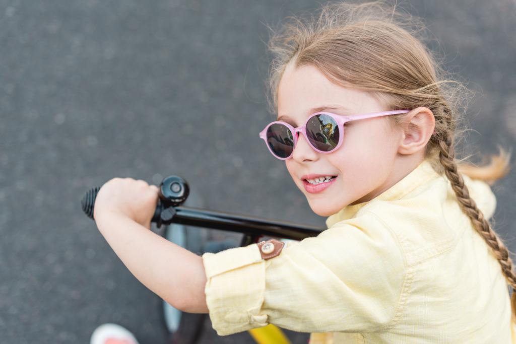 γκρο πλαν θέα της χαριτωμένο χαμογελαστό παιδί σε γυαλιά ηλίου ιππασία ποδήλατο  - Φωτογραφία, εικόνα
