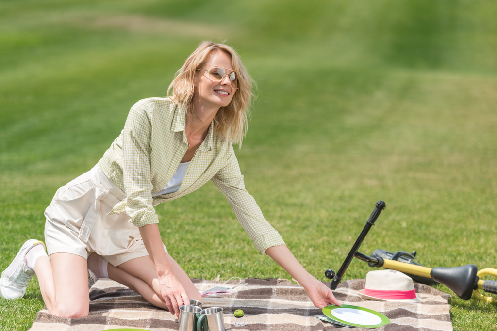 onnellinen nuori nainen laittaa ruokailuvälineet ruudullinen piknikillä
  - Valokuva, kuva
