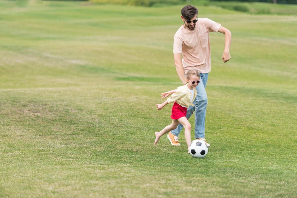 ευτυχισμένος πατέρας και η μικρή της κόρη παίζει με την μπάλα ποδοσφαίρου στο πάρκο - Φωτογραφία, εικόνα