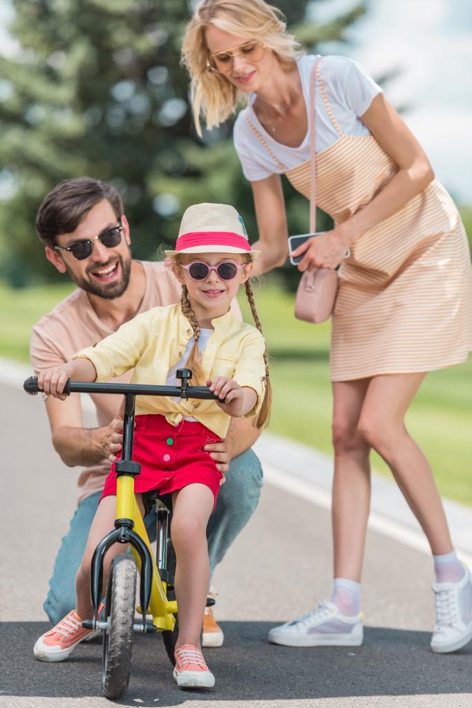 Glückliche Eltern betrachten süße kleine Tochter beim Fahrradfahren im Park - Foto, Bild