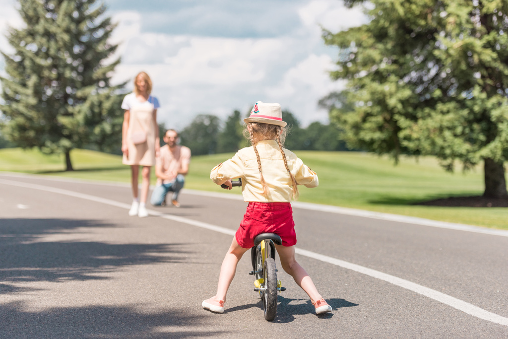 вид ззаду на дитячий велосипед і батьків, що стоять позаду в парку
 - Фото, зображення