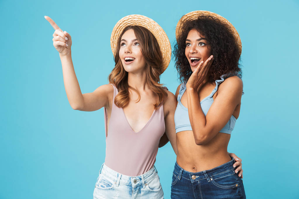 Deux jeunes filles excitées habillées en vêtements d'été pointant vers l'espace de copie isolé sur fond bleu
 - Photo, image