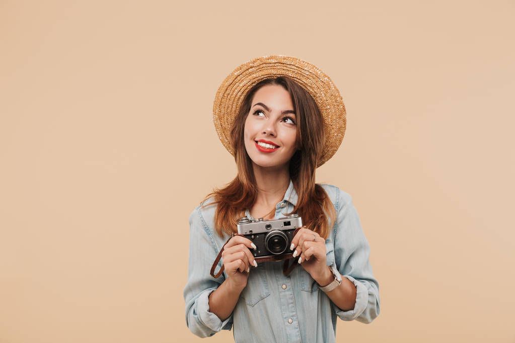 Portrét usměvavá mladá dívka drží fotoaparát a při pohledu na kopie prostoru izolované béžové pozadí - Fotografie, Obrázek