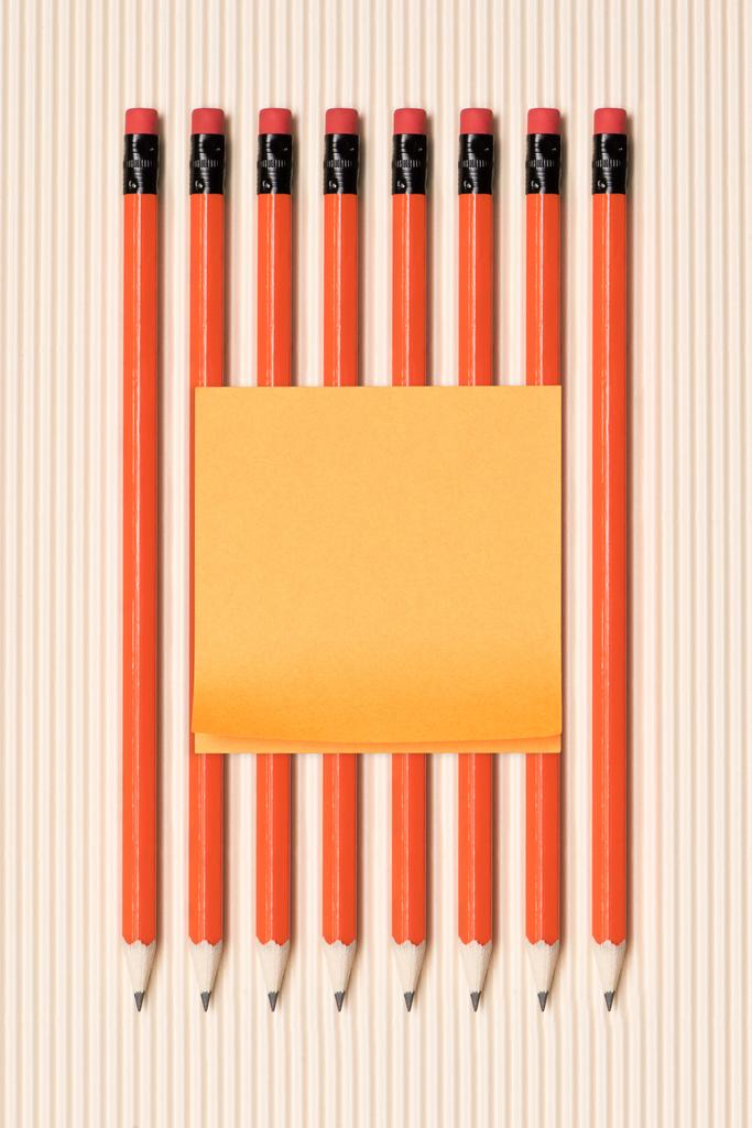 верхний вид пустой палки это записка на графитовые карандаши с ластиками помещены в ряд на бежевый
  - Фото, изображение