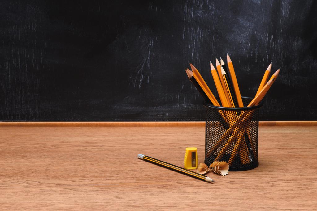 close up view of desk organizer with pencils and sharpener on wooden table in front of empty chalk board in school - Photo, Image