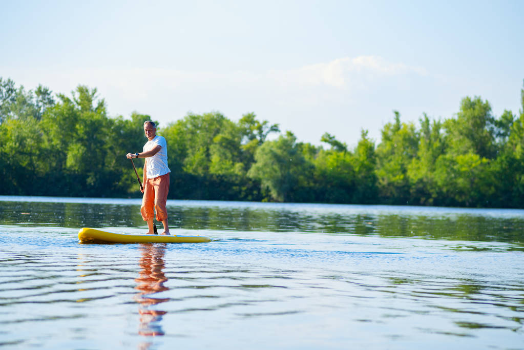 Radosny człowiek żagle na desce Sup w dużej rzeki w słoneczny poranek. Stand up paddle boarding - niesamowite aktywnego wypoczynku na świeżym powietrzu.  - Zdjęcie, obraz