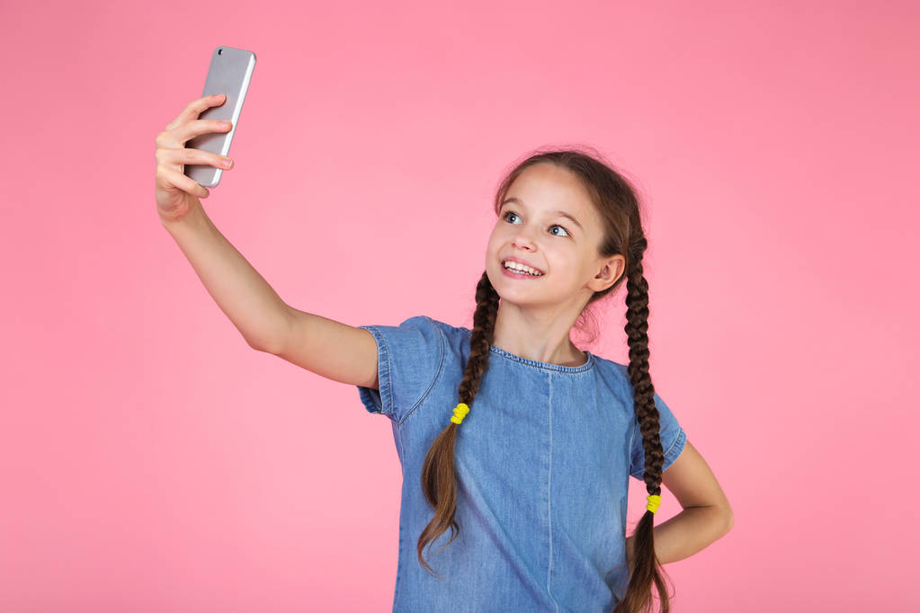 Young girl in denim dress making selfie on pink background - Photo, Image