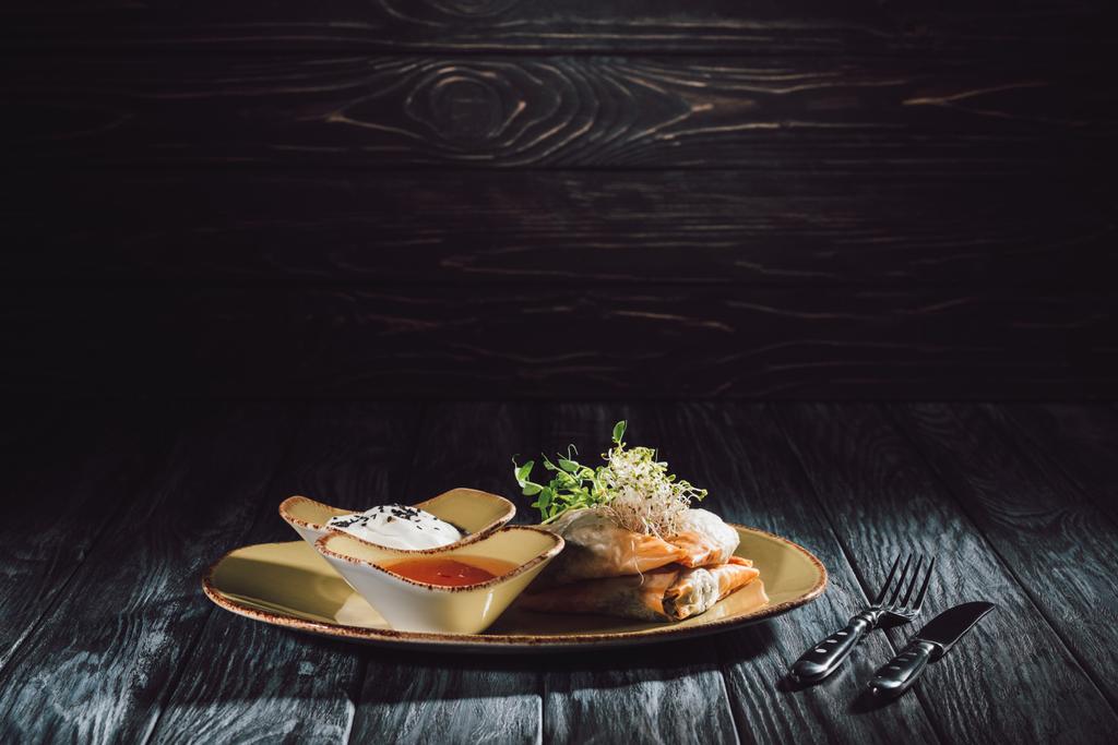 Samosa in filodeeg deeg gevuld met spinazie en paneer versierd met ontkiemde zaden van luzerne en zonnebloem op plaat in de buurt van vork met mes op houten tafel - Foto, afbeelding