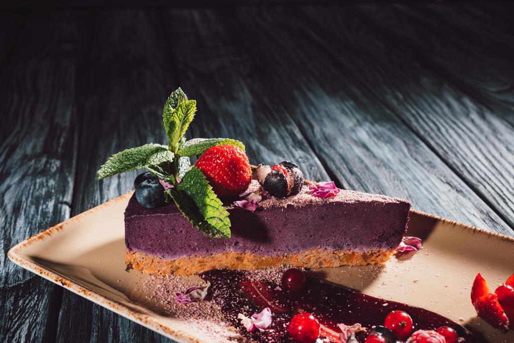 vista de cerca de pastel de arándanos con fresas, menta y pétalos de viola en el plato en la mesa de madera
  - Foto, Imagen
