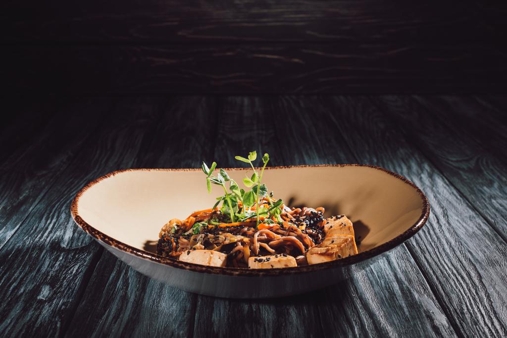soba com tofu e legumes decorados com sementes germinadas de girassol na placa na mesa de madeira
  - Foto, Imagem