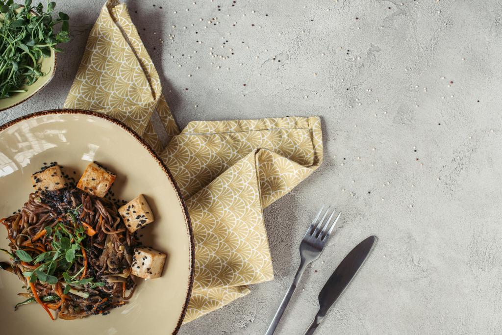 Essenszusammensetzung mit Soba mit Tofu und Gemüse, dekoriert mit gekeimten Sonnenblumenkernen auf grauer Tischplatte - Foto, Bild