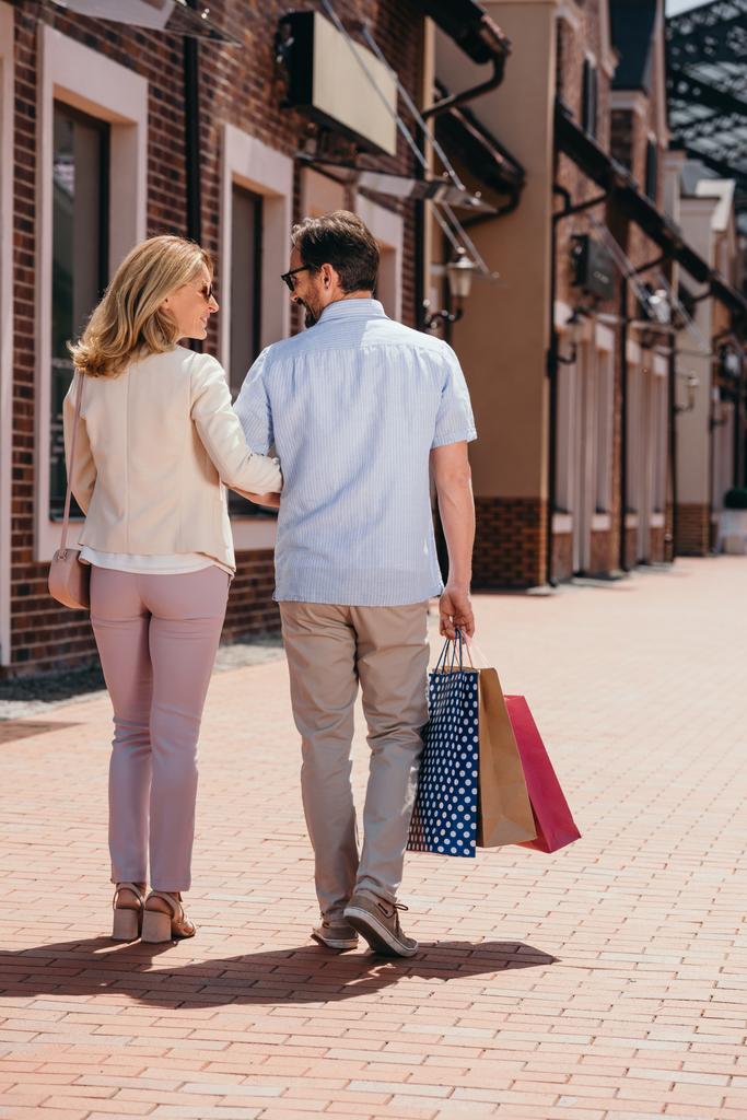 Rückansicht eines Paares, das mit Einkaufstüten auf der Straße spaziert - Foto, Bild